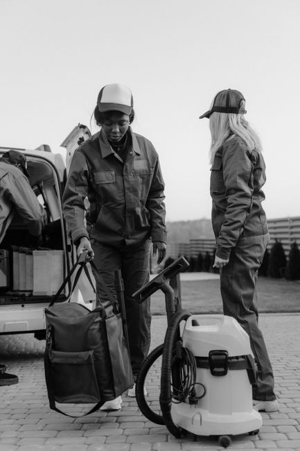 Two professional cleaners from Hackney Cleaner are performing surface cleaning in a modern living room. The cleaner on the left, a woman with blonde hair, is operating a yellow vacuum cleaner on a lig